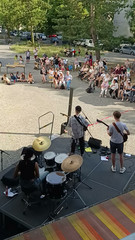 Eine Band spielt auf einer Musikbühne vor zahlreichen Menschen beim Musikfestival Fête de la Musique auf dem Platz vor dem Immanuel Stadtteilzentrum Borsigwalde in Berlin-Reinickendorf.