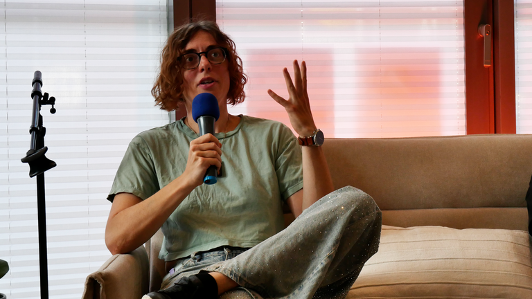 Alex M. Gastel spricht mit Mikrofon auf einer Couch Alex M. Gastel spricht mit Mikrofon auf einer Couch