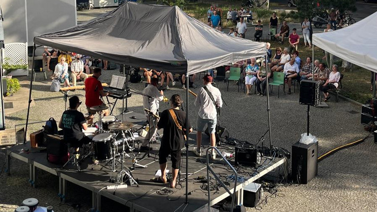 Blick auf die überachte Bühne mit einer Band vor Publikum über den Platz beim Musikfestival Fête de la Musique vor dem Immanuel Stadtteilzentrum Borsigwalde in Berlin-Reinickendorf.
