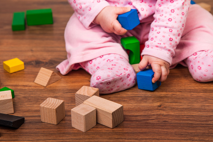 Ein Kleinkind sitzt mit einem hellpinken Overall auf einem Holzboden und spielt mit bunten Holzklötzen als Motiv für den Kurs für Eltern mit Baby FuN-Baby der Immanuel Beratung Fennpfuhl mit dem Kinder-und Jugendgesundheitsdienst Lichtenberg (KJGD) in Berlin. Ein Kleinkind sitzt mit einem hellpinken Overall auf einem Holzboden und spielt mit bunten Holzklötzen als Motiv für den Kurs für Eltern mit Baby FuN-Baby der Immanuel Beratung Fennpfuhl mit dem Kinder-und Jugendgesundheitsdienst Lichtenberg (KJGD) in Berlin.