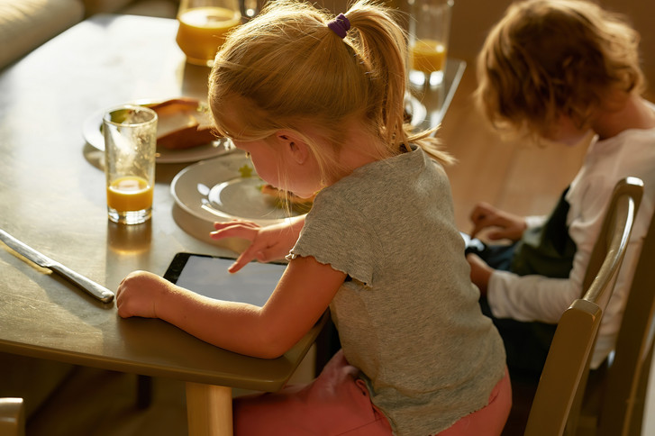 Mädchen und Junge sitzen an einem Esstisch und blicken auf eien Tablet und ein Handy - Immanuel Beratung Buch - Elternabend zum Thema Medienkonsum bei Kindern