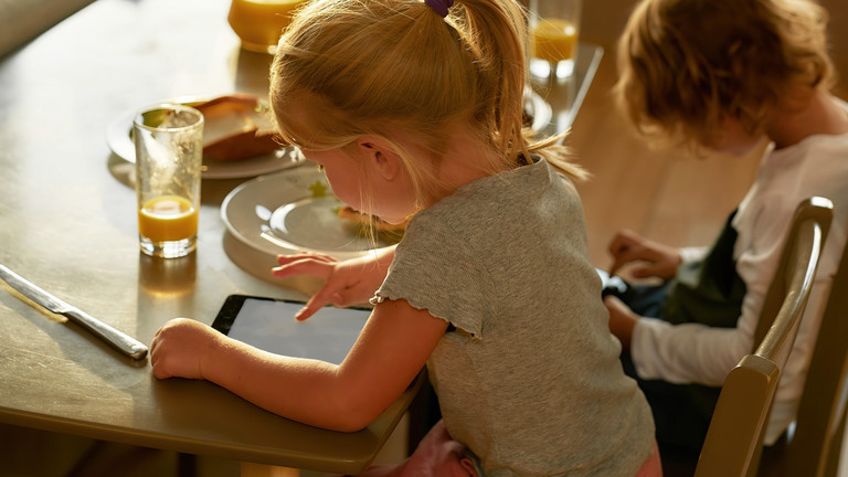 Mädchen und Junge sitzen an einem Esstisch und blicken auf eien Tablet und ein Handy - Immanuel Beratung Buch - Elternabend zum Thema Medienkonsum bei Kindern